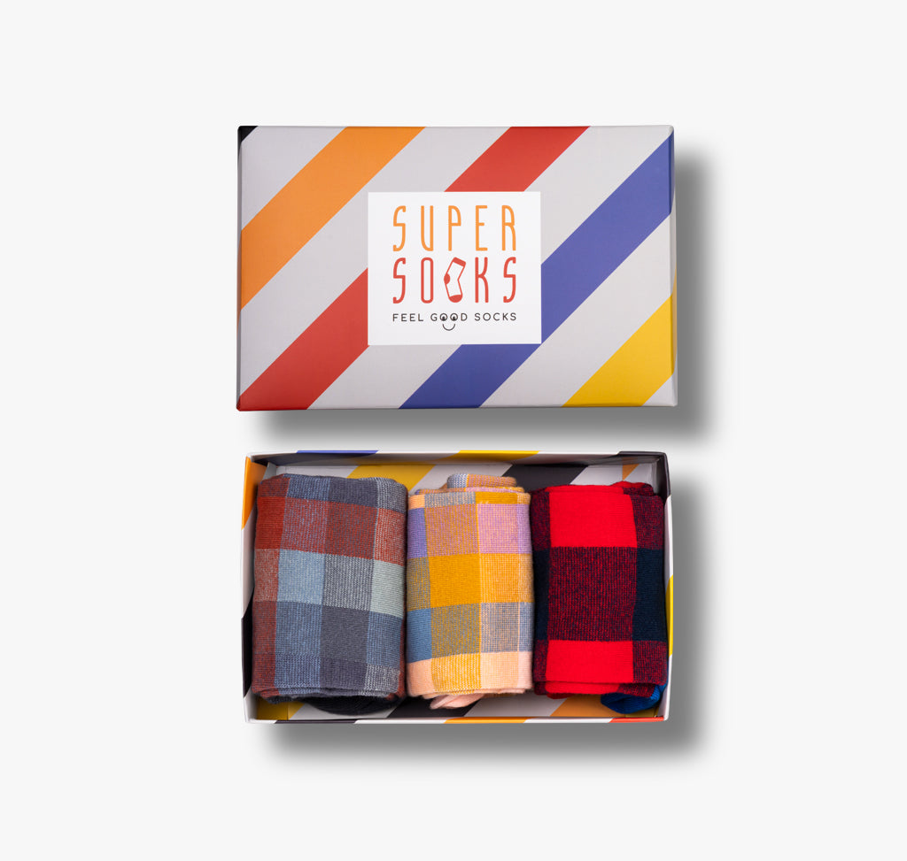 In einer gestreiften Geschenkbox verpackt sind drei Paar bunte Socken mit quadratischen Mustern passend für Damen und Herren